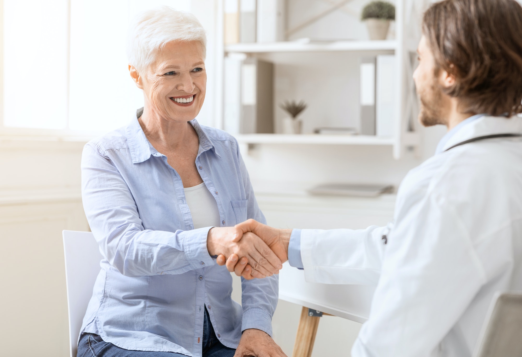 Happy senior woman handshaking with personal doctor at office